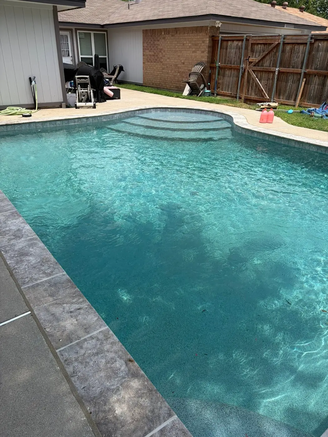 A rectangular backyard pool with clear water, patio furniture and shade trees, kept by weekly Kingdom Pools service