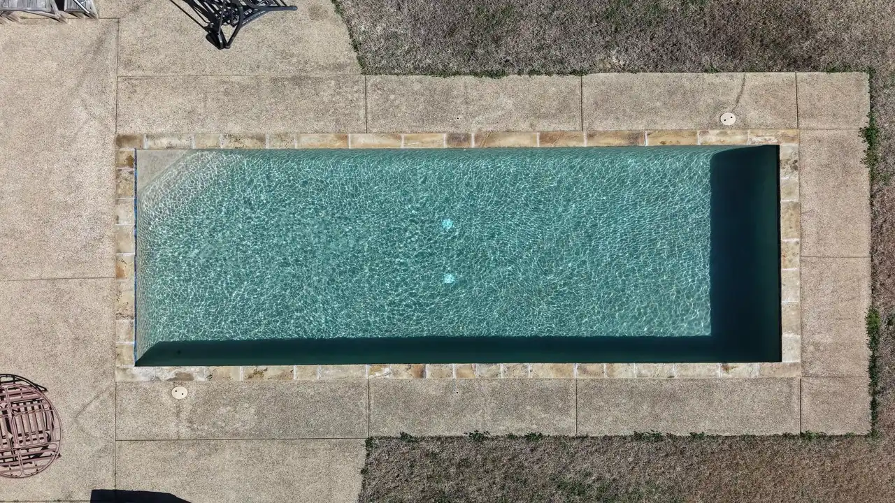 Aerial view of a rectangular backyard pool with clear water and a clean concrete deck